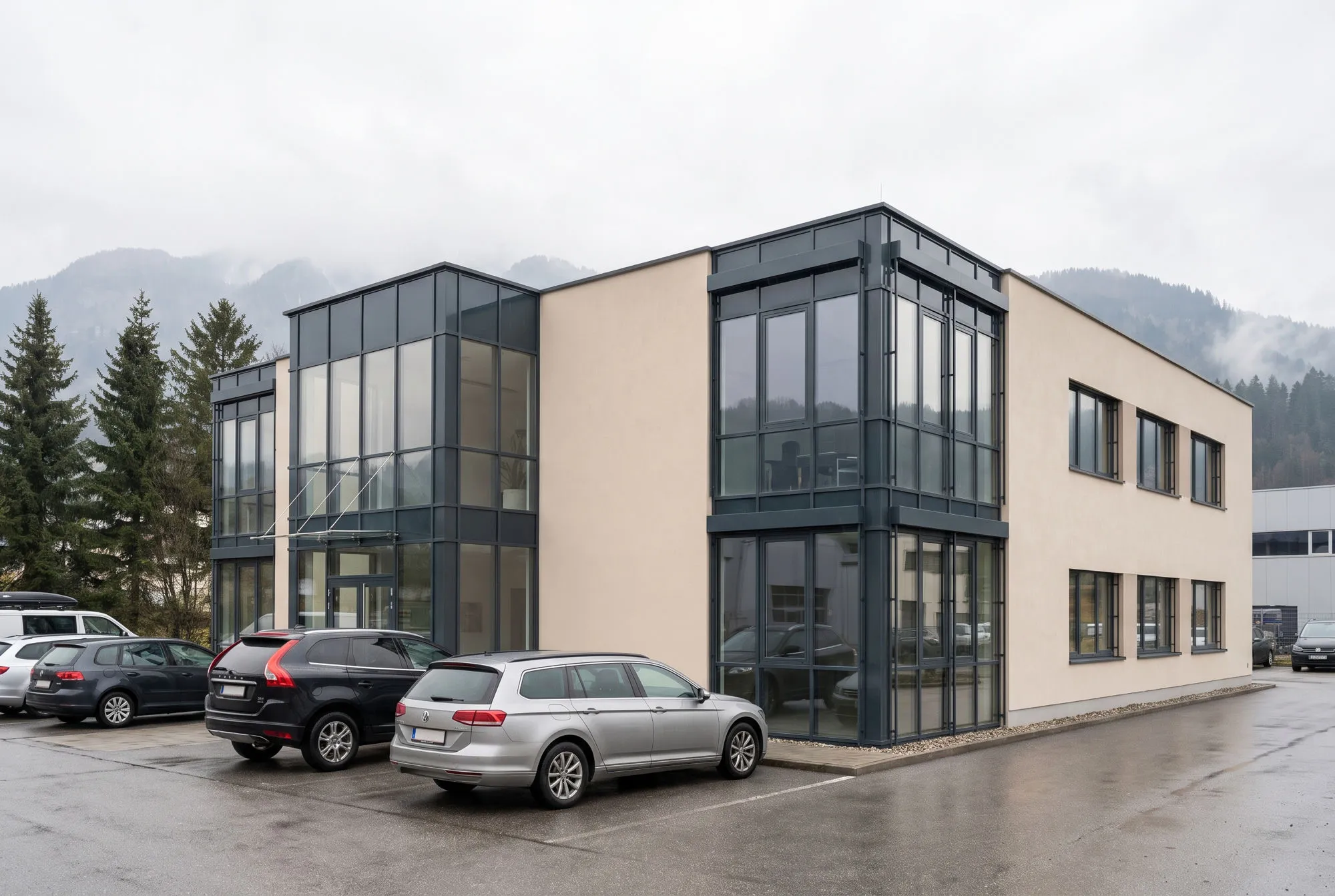 A two-storey office building of glass and pale render in an alpine business park.
